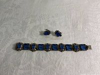 Top view of sterling silver bracelet and matching earrings with blue rectangular stones on white textured fabric.