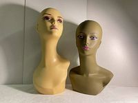 Front view of both wig mannequin heads showing painted facial features and neck length difference.