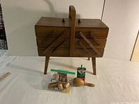 Full view of vintage accordion sewing box standing on legs with sewing items in front
