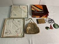 Full lot view showing clutch purse, Leonardo scarf, two sets boxed handkerchiefs, enamel pendants, brooch, and compact.
