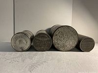 Four vintage kitchen tins arranged in a row showing the tops. Embossed and printed brand/product information visible for identification.