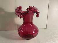 Side view of the vintage cranberry glass vase showing its bulbous body and ruffled top edge.