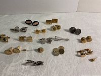 Photo showing 18 pieces of vintage cuff links arranged on white background with various metallic finishes and designs.
