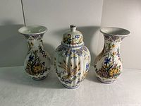 Front view of the full set showing two trumpet vases and a lidded urn with ornate hand-painted floral and wheat patterns.