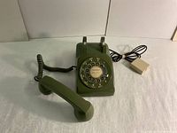 Front view showing the rotary dial, handset off the cradle, and telephone line cable with beige plug