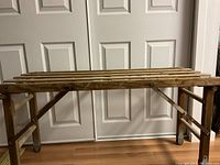 Full view of the assembled vintage wooden wash stand with slatted top and spindle sides on hardwood floor in front of white doors.