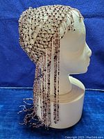 Side view of the flapper headdress on a mannequin head, showing bead netting and hanging bead fringe.