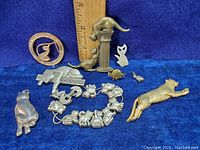 Photo showing a collection of cat-themed jewelry pieces including brooches, charms, and a bracelet. A ruler is placed for size reference.