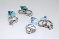 Four sterling silver rings laid out showing tags and styles including solitaire, floral cluster, and channel set stones.