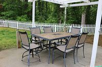 Front view showing table and six chairs under pergola on concrete patio