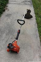 Full view of the curved shaft string trimmer with orange gas engine housing and black handle.
