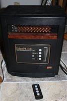 Front view of the black EdenPURE GEN4 heater with remote placed in front, showing control panel and vent area with heating elements visible.