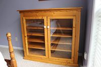 Front view of large oak cabinet showing double glass doors, four shelves inside and scalloped trim.