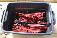 Large plastic tub filled with predominantly red and some black plastic tie wraps in various lengths.