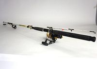 Offshore Angler Power Stick surf spinning rod with black foam handles and line guides, laid out on a white surface with a spinning reel attached.