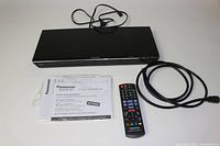 Panasonic Blu-Ray player laid flat with accompanying remote, power cord, HDMI cable, and product information sheets arranged beneath.