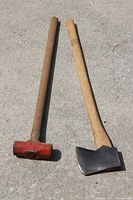 Photo showing the full sledge hammer and axe side by side on a concrete surface, highlighting their overall shape, handles, and heads.