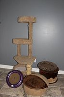 Full view of the staggered beige cat tree with two platforms, the two cat beds, one plush brown round and one leopard print footstool style, and purple circular cat toy with balls inside.