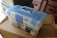 Closed view of a clear plastic toolbox with blue handle and latch sitting on a cardboard box.