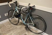Full side view of light blue Trek road bike leaning against wall with two helmets hanging on top tube.