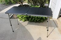 Folding camping table fully opened, showing black table surface and metal legs.