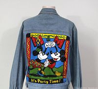 Back of denim jacket showing colorful Mickey and Minnie Mouse dancing graphic with "It's Party Time" text.