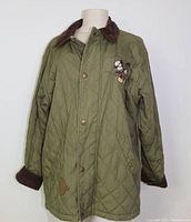 Front view of olive green quilted chore jacket with brown corduroy collar and cuffs, featuring embroidered Mickey Mouse on the chest and angled front pockets.