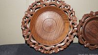 Close up of one hand carved wooden plate showing intricate floral and leaf design around the circular rim, with smooth center and concentric rings