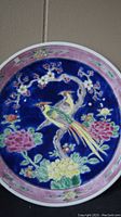 Front view of the antique hand painted decorative plate showing bird and floral design with dark blue background and pink rim.