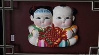 Close-up of two Chinese Clay Fu dolls mounted together holding a red good luck knot.