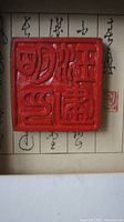 Close-up photo of the red Chinese seal stamp showing carved characters with glossy finish.