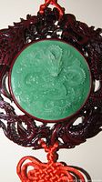 Close-up photo of the green jade circular medallion carved with a detailed dragon, mounted on dark wood carved dragon frame with red hanging cord.
