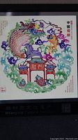 Close-up photo of the Chinese paper cut artwork showing dragon, fish, clouds, and traditional structures.