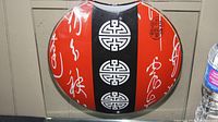 Glass art holder showing red, black, and white circular plaque with Chinese symbols and calligraphy.