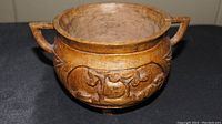Close up photo of the hand carved wooden pot showing detailed animal carving and the pot's handles and feet.
