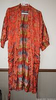 Front view of long women's nightwear robe made of silk fabric in orange and multicolor pattern with two front pockets and slight cuffed sleeves.