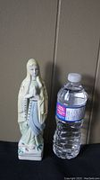 Front view of the hand painted religious statue standing next to a water bottle for scale.