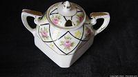 Square porcelain sugar bowl with lid, hand painted pink roses and small yellow flowers, green diamond design, gold trim on edges and lid knob against black background