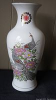 Front view of large white porcelain vase showing colorful peacock and floral painting with emblem near neck.