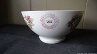 Side view of white porcelain rice bowl showing hand-painted roses in baskets and pink decorative circular seals with Chinese characters.