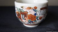 Close-up side view of one porcelain teacup showing detailed hand-painted floral and fan decoration with Japanese script.