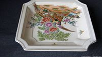 Angle view of square porcelain plate showing intricate hand-painted birds and floral motif on cream background, highlighting plate shape and ornate edges.