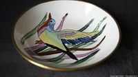 Close-up of the inside of the bowl showing a colorful hand painted bird and grass design with a brass rim.