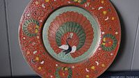 Photo of round brass enamel cloisonné plate showing central peacock and detailed colorful floral border