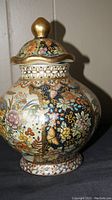 Front angle of porcelain jar with detailed floral and butterfly decoration and gold accented lid in place.
