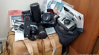 Group shot of cameras, lenses, motor drive, bags, filter pack and manuals on tan leather carry bag