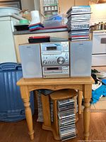 Full view of Sony Micro Hi-Fi system with two speakers on wooden side table, CD holder underneath, and stacks of CDs on countertop