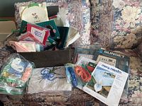 Box containing assorted cross stitch fabrics, threads, and partially completed embroidery