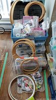 Blue tote bin filled with small pink and clear thread organizers, wooden hoops stacked on top