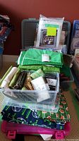 Clear plastic bin filled with folded fabrics including green solids and bee-themed packs atop pink bin with Seahawks fabric underneath